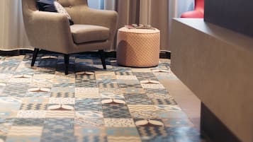 A room with a patterned floor, a tufted armchair, a round ottoman, and a reception desk.