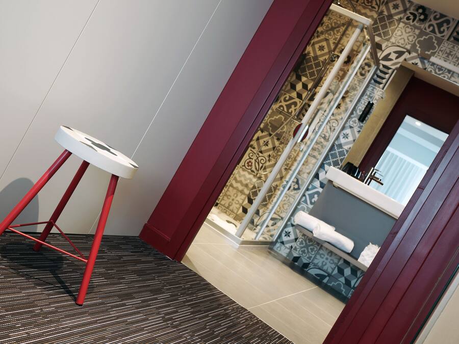 Un baño moderno con baldosas estampadas, un lavamanos blanco y un taburete rojo.
