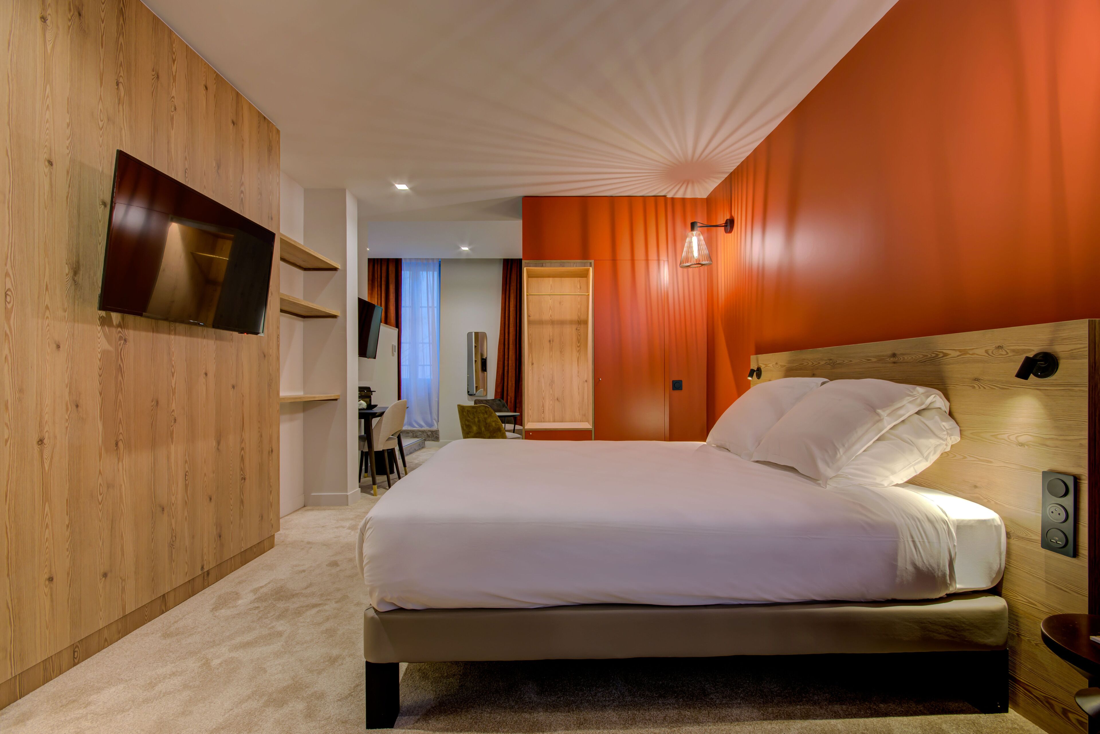 Una habitación de hotel moderna con una cama grande, paneles de madera, un televisor de pantalla plana y cabecero de madera.