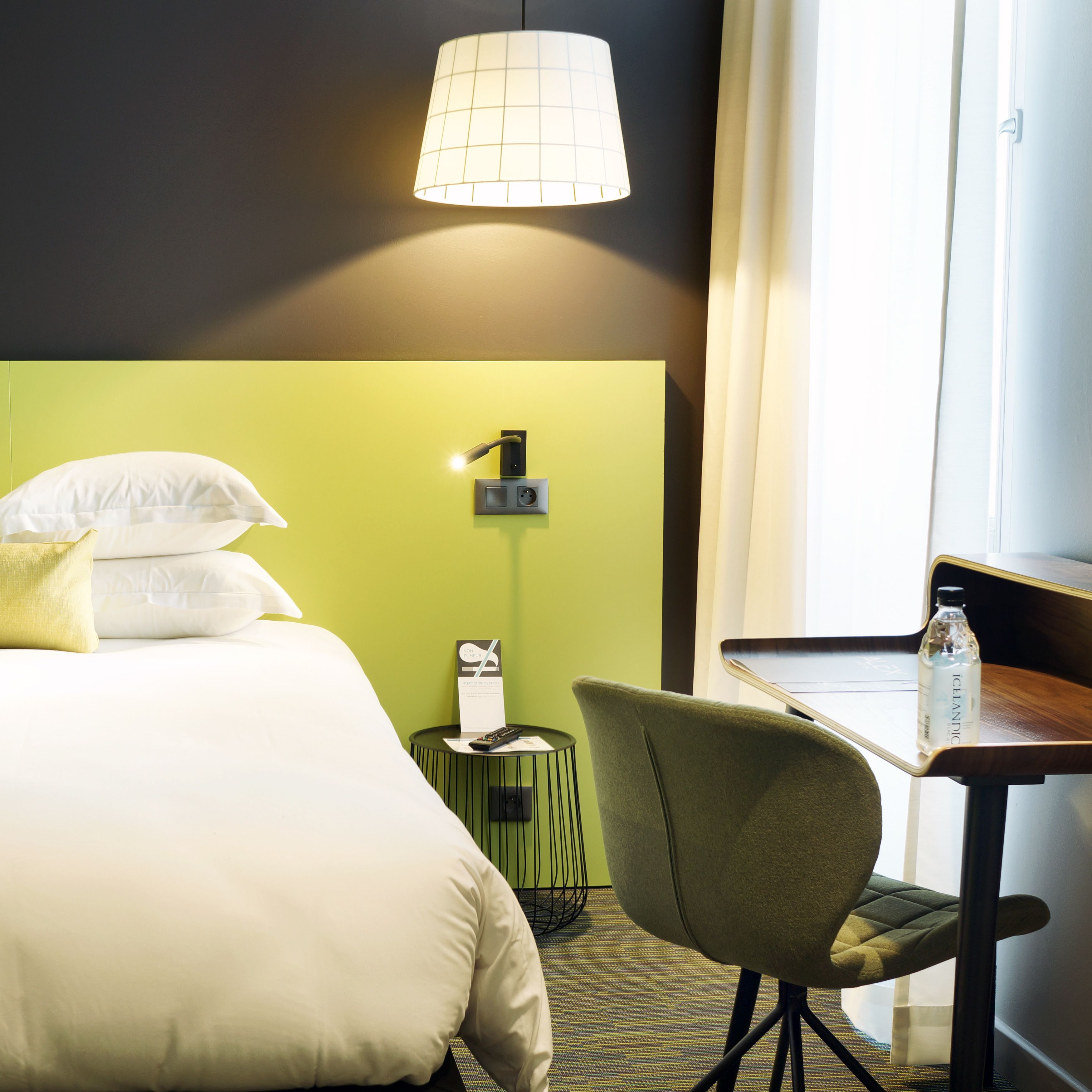 Una habitación de hotel con una cama, un escritorio, una silla, una lámpara y una botella de agua.