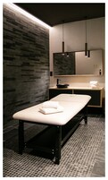 Un baño moderno con pared de piedra, un banco, un lavamanos y un espejo.