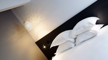 Un lit bien fait, avec du linge de lit blanc et des oreillers, une suspension lumineuse et un tableau encadré au mur.