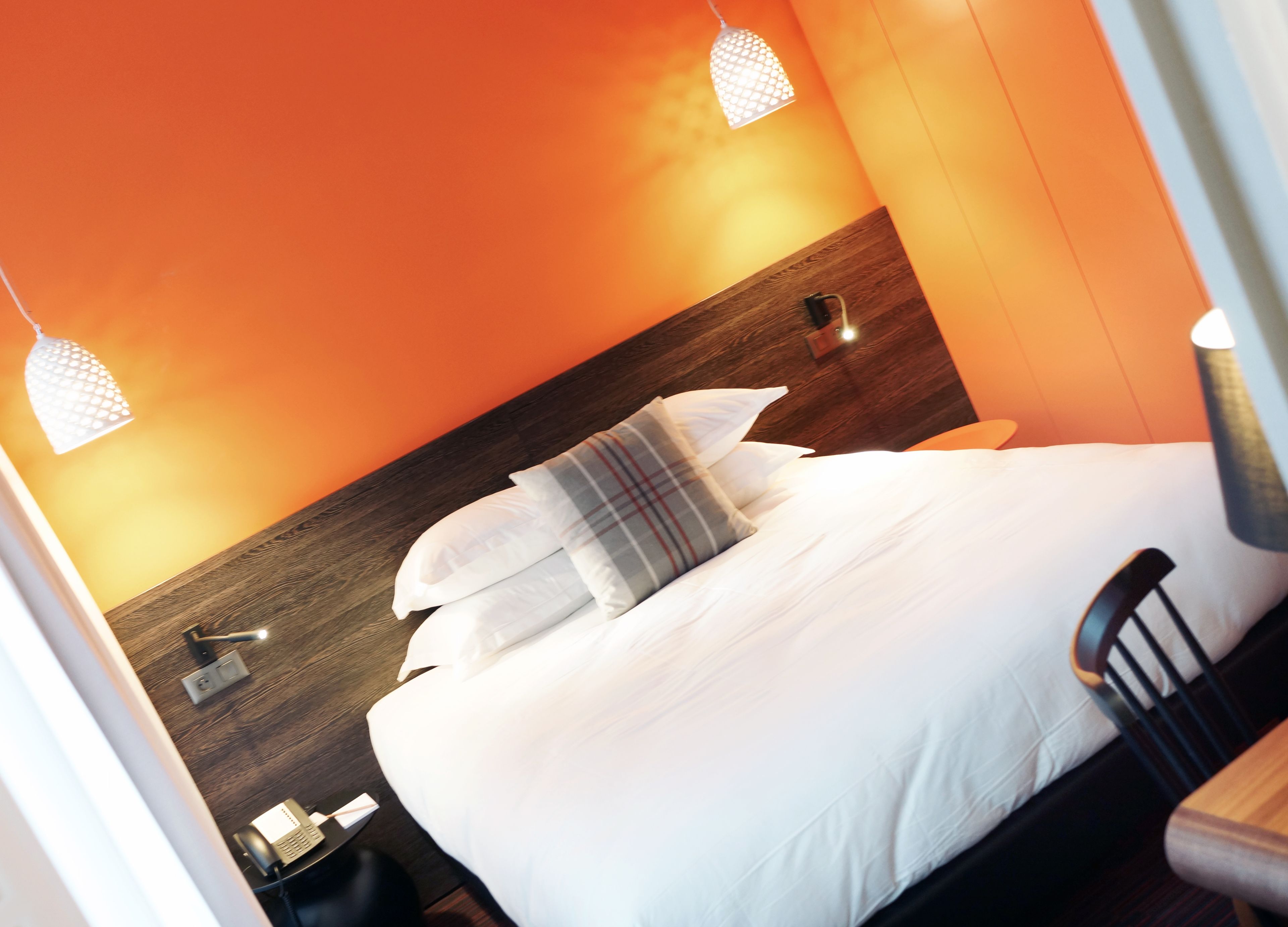 Une chambre d’hôtel avec une tête de lit en bois, un lit avec une literie blanche et des oreillers à carreaux, une table de chevet avec une lampe et un téléphone.