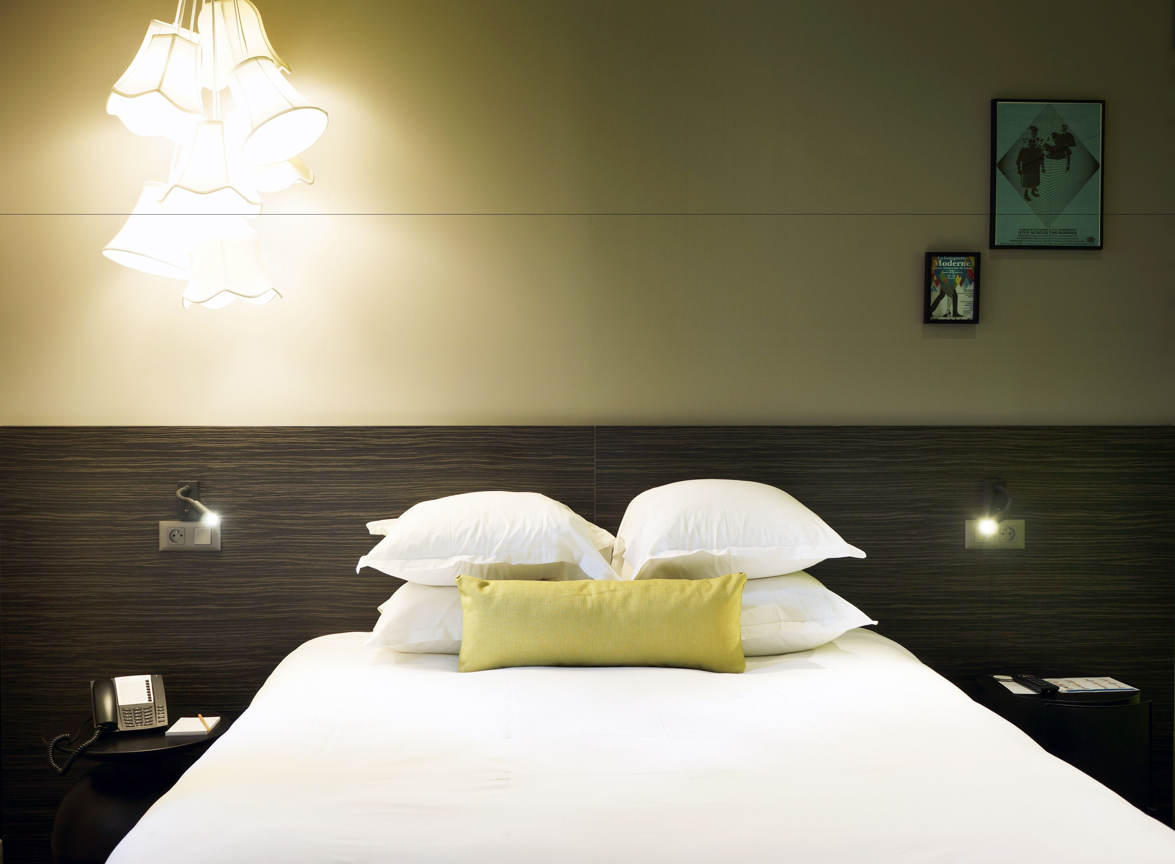Een hotelkamer met een opgemaakt bed, een telefoon op het nachtkastje en een wandlamp.