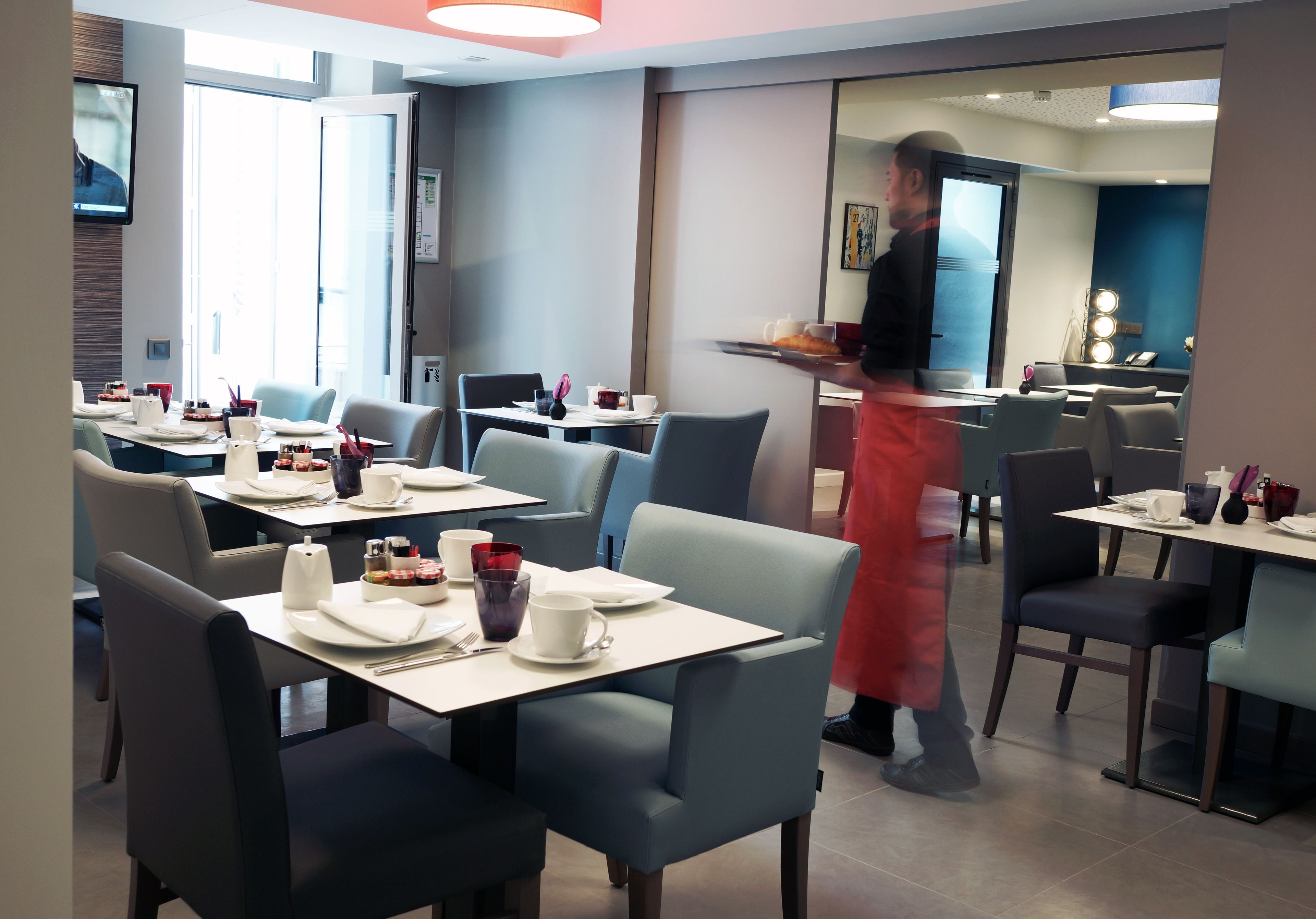 A modern restaurant with tables set for dining, a waiter in uniform, and a visible reception area.