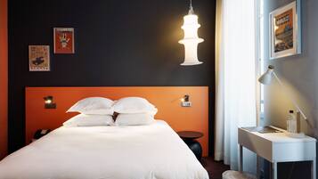 Ein Hotelzimmer mit einem großen Bett, einem Schreibtisch mit Stuhl, einer Hängelampe und einem gerahmten Bild an der Wand.