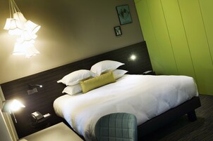 A neatly made bed with white linens and a green pillow, a bedside lamp, a phone, and a framed picture on the wall.