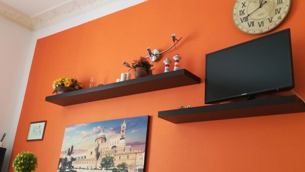 Une pièce aux murs orange, avec une horloge, un téléviseur et deux tableaux.