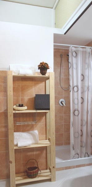 Een badkamer met een houten plankunit, een douche met een decoratieve gordijn en een betegelde muur.