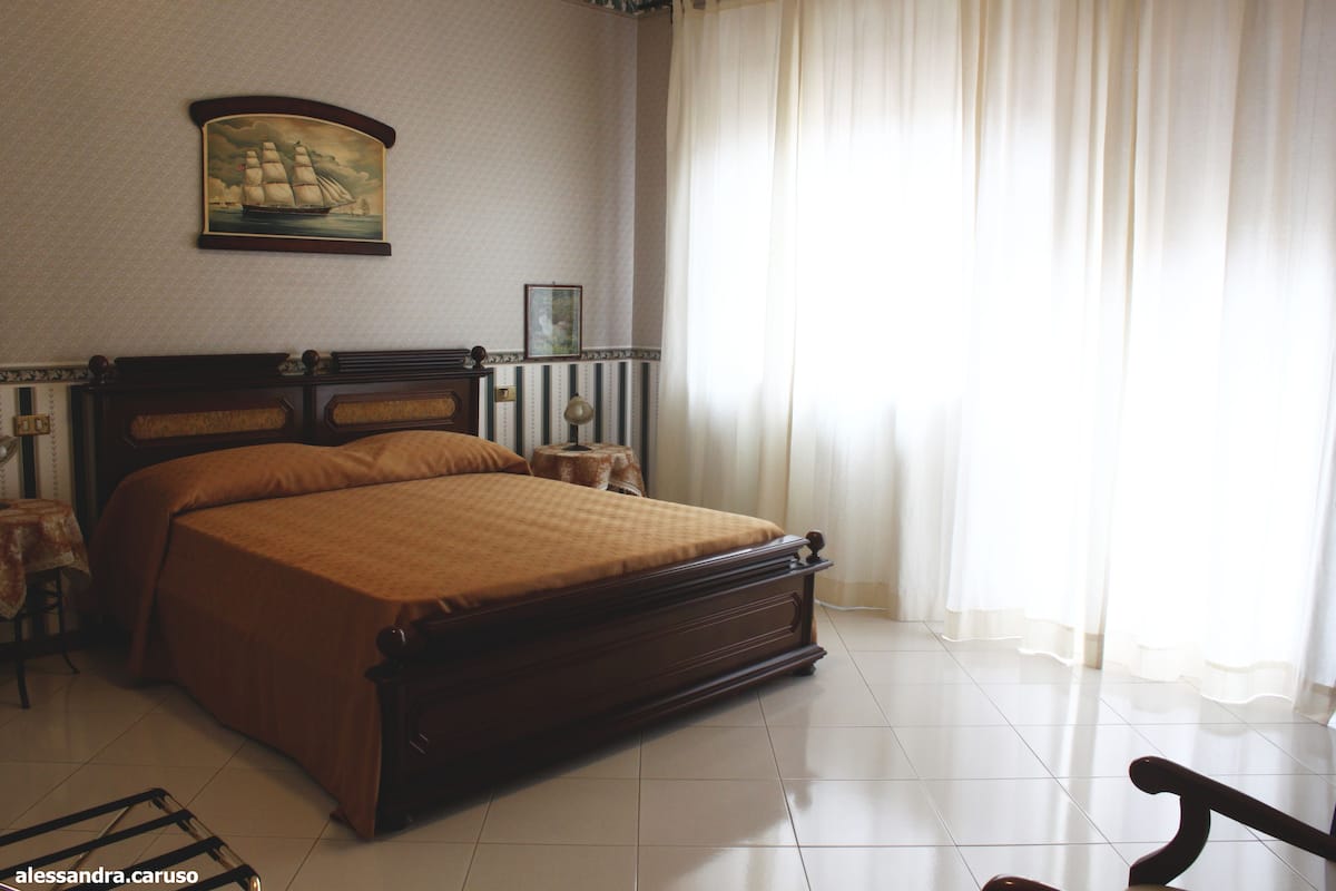 A neatly arranged bedroom with a large bed, a bedside table, a lamp, and a framed picture on the wall.
