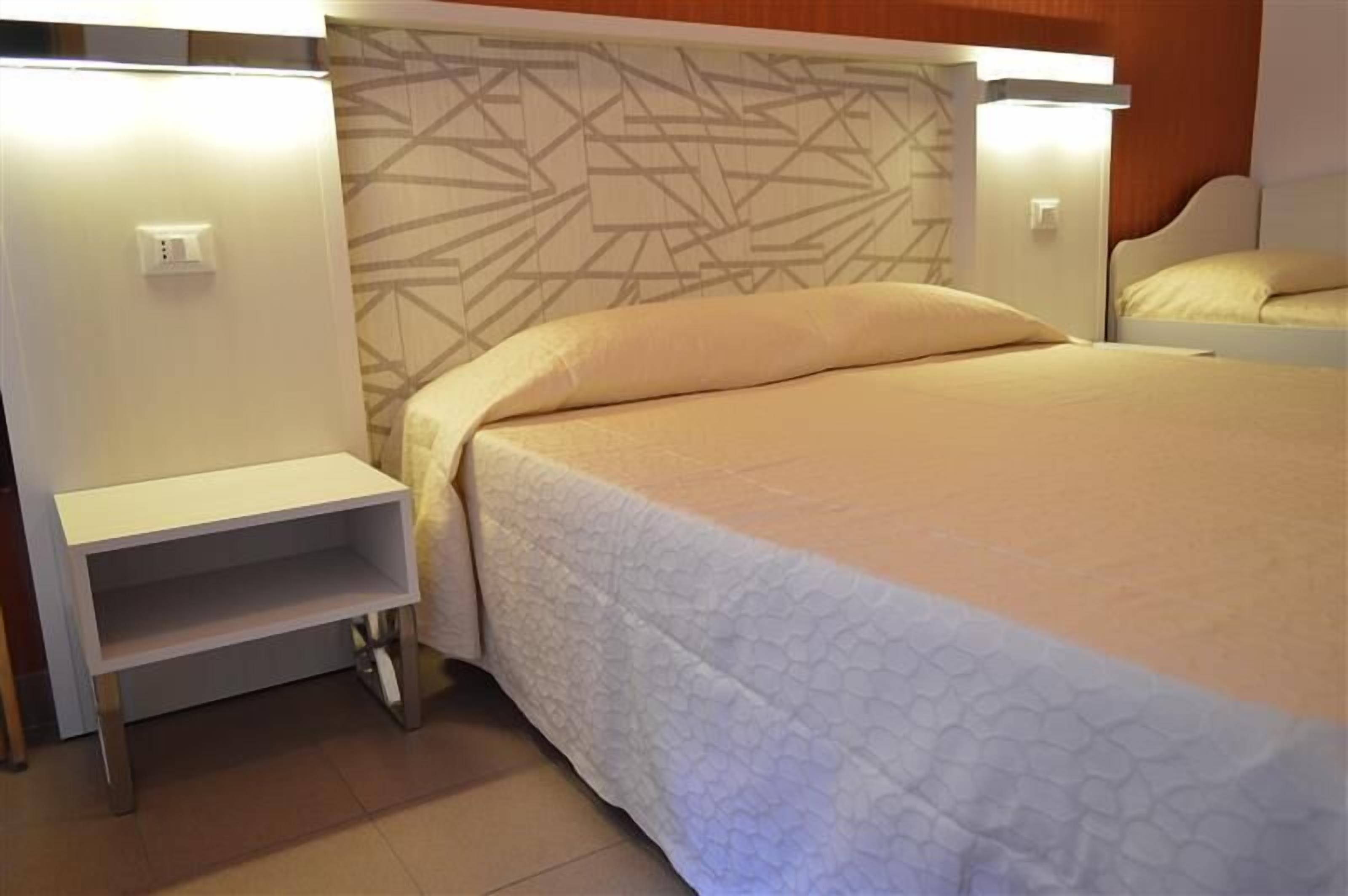 A hotel room with a bed, a bedside table, and a wall-mounted shelf.
