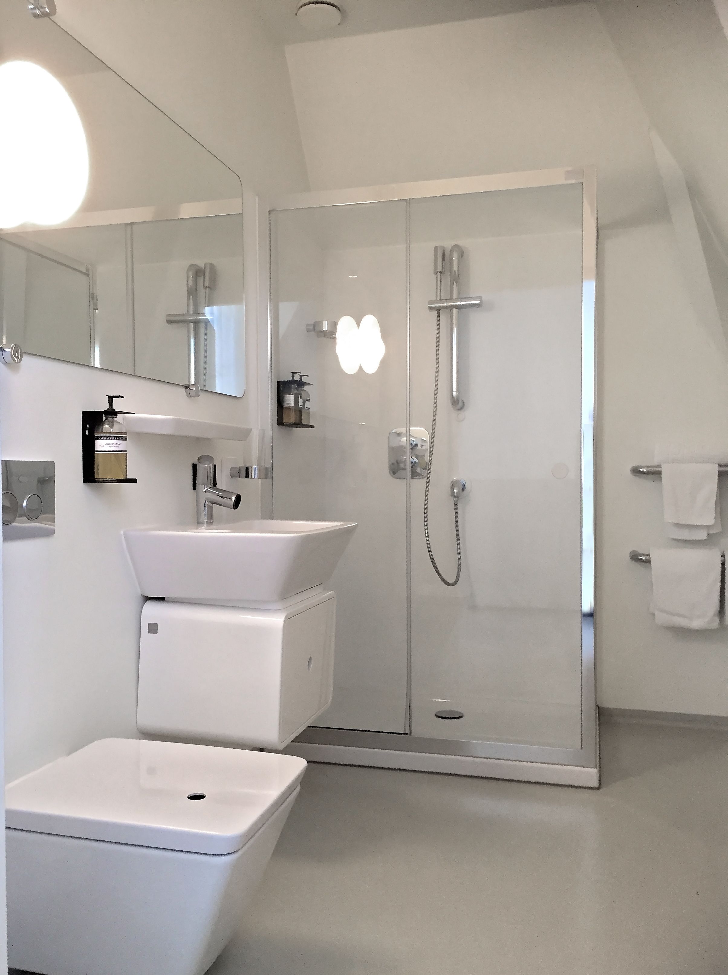 Un baño moderno con ducha separada por vidrio, un lavabo blanco y un espejo grande.