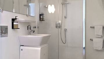 Un baño moderno con ducha separada por vidrio, un lavabo blanco y un espejo grande.