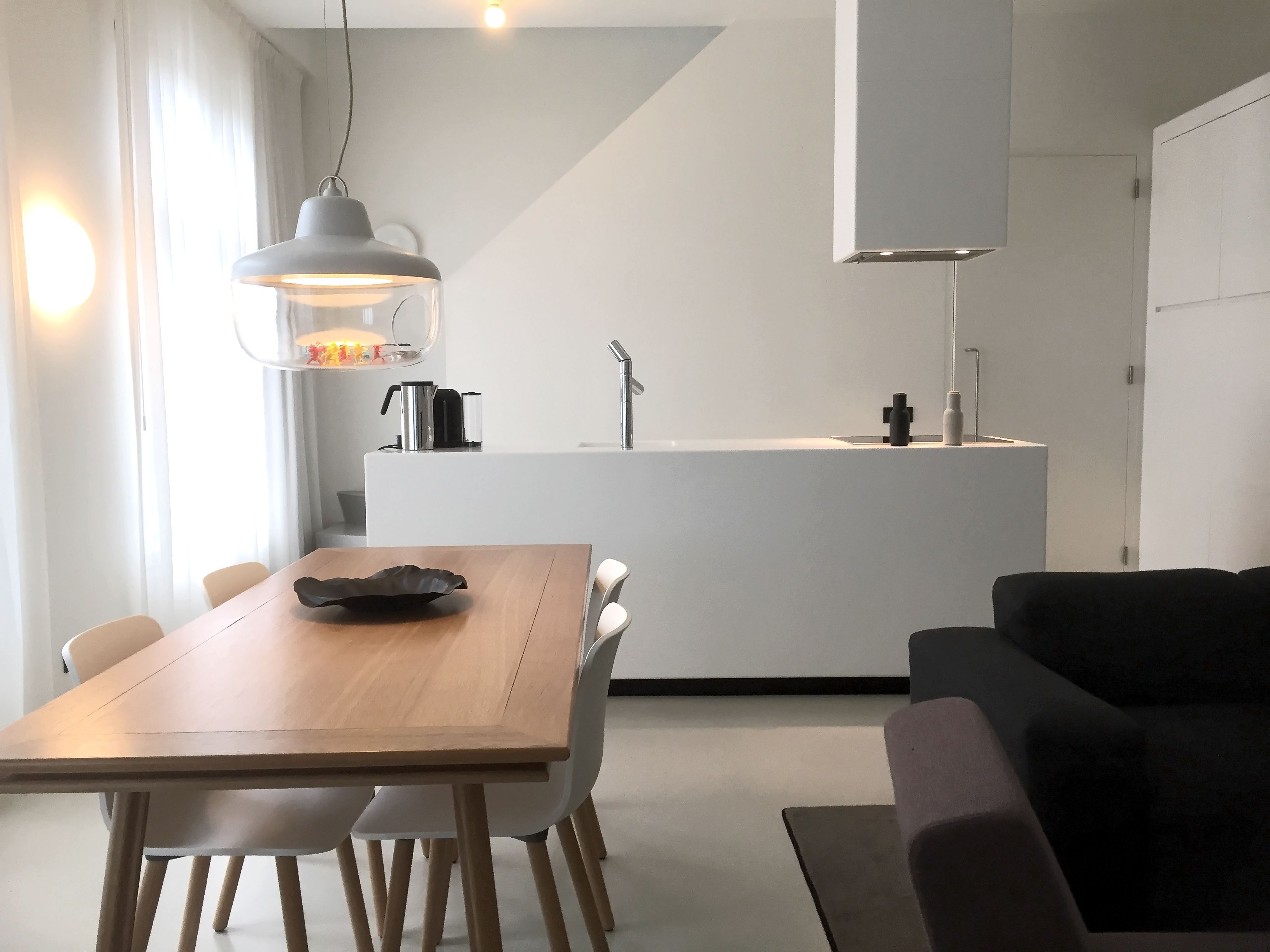 A modern kitchen with a central island, a dining area with a wooden table and chairs, and a black sofa in a living area.