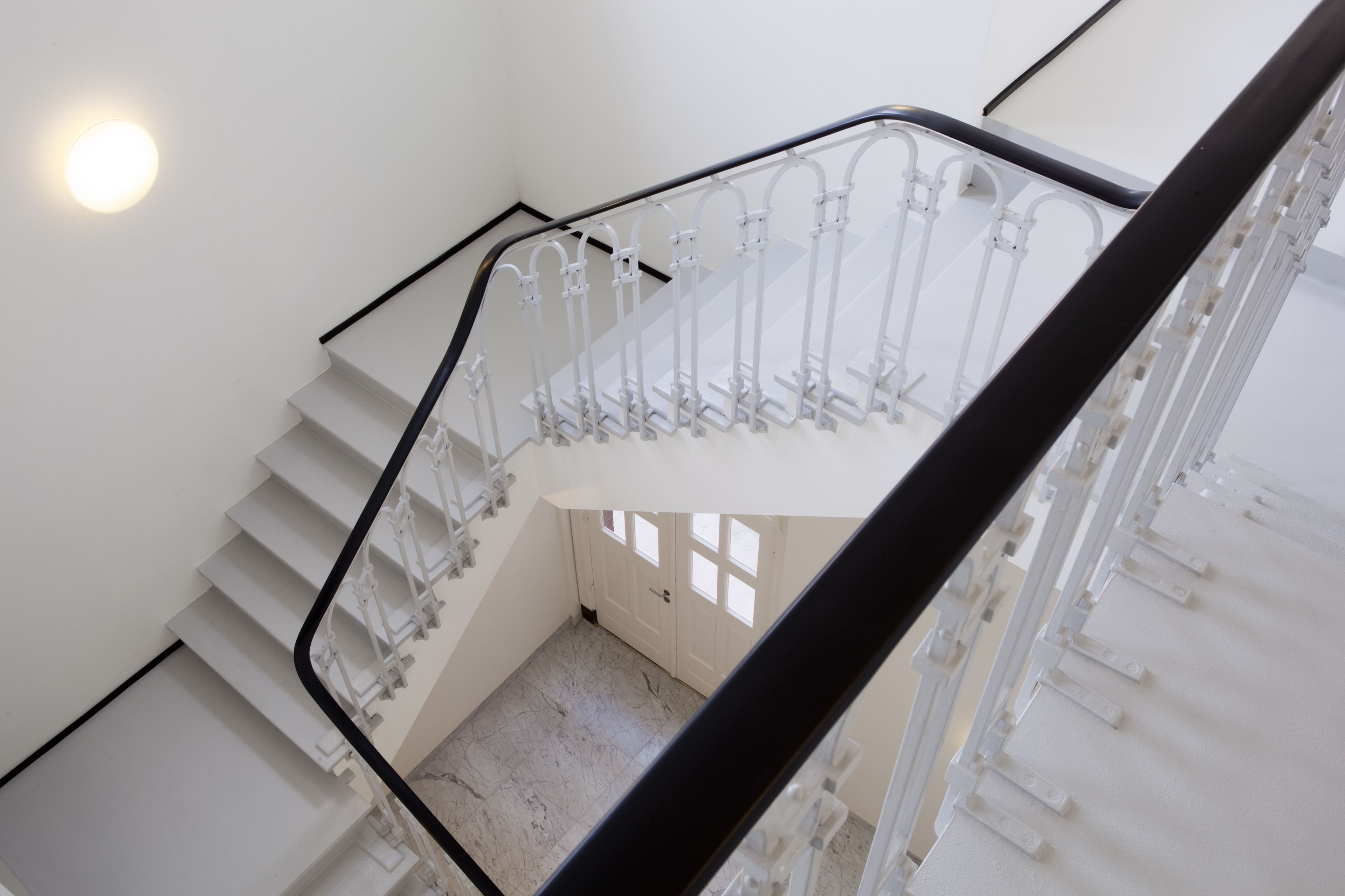 A staircase with white railings and a black handrail, leading to a landing with a door and windows.