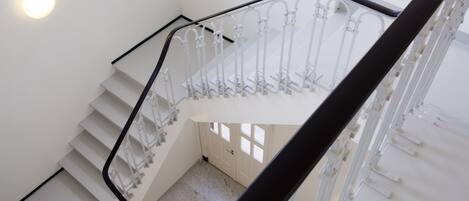 A staircase with white railings and a black handrail, leading to a landing with a door and windows.