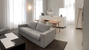 Una sala de estar moderna con un sofá gris, una pequeña mesa de comedor y una zona de cocina al fondo.