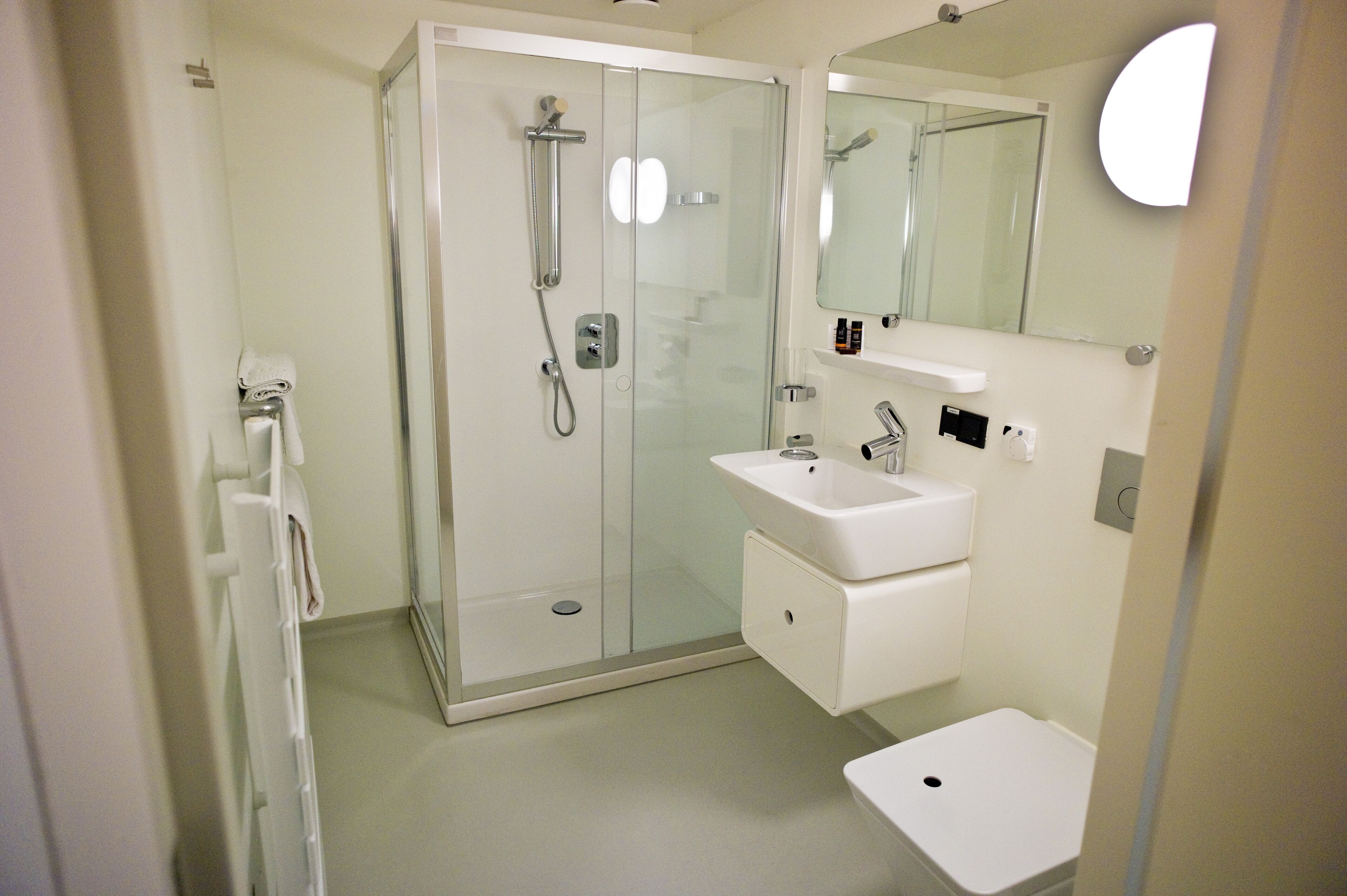 Ett modernt badrum med en dusch som är avskärmad med glasväggar, en vit tvättställ och en spegel ovanför tvättstället.