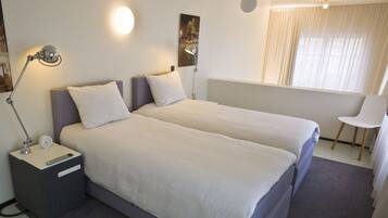 Ein Hotelzimmer mit zwei Betten, einem Nachttisch mit Lampe, einem Sessel und einem Fenster mit Vorhängen.