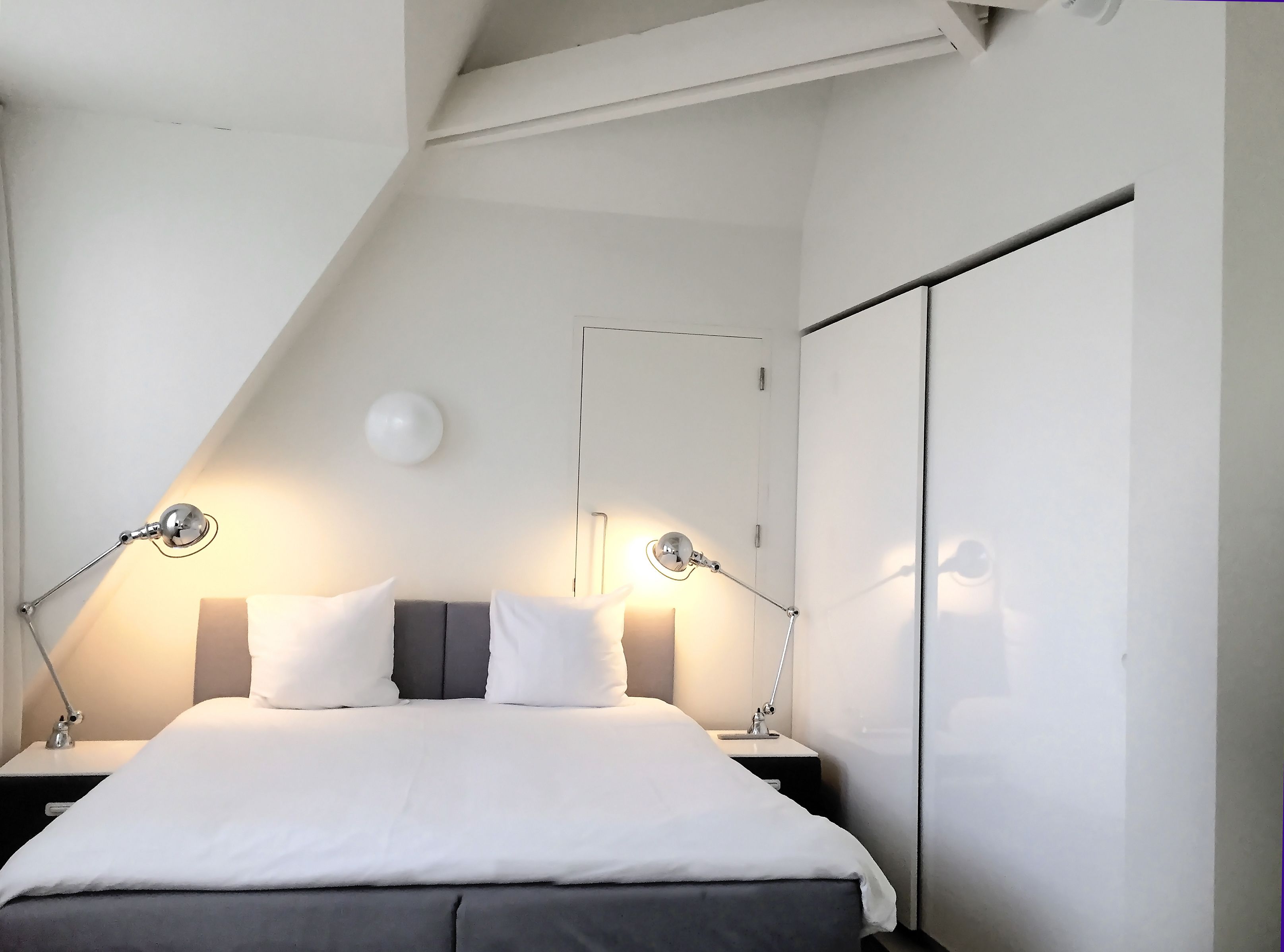 Un dormitorio moderno con cama, dos lámparas de noche, un reloj de pared y un armario.