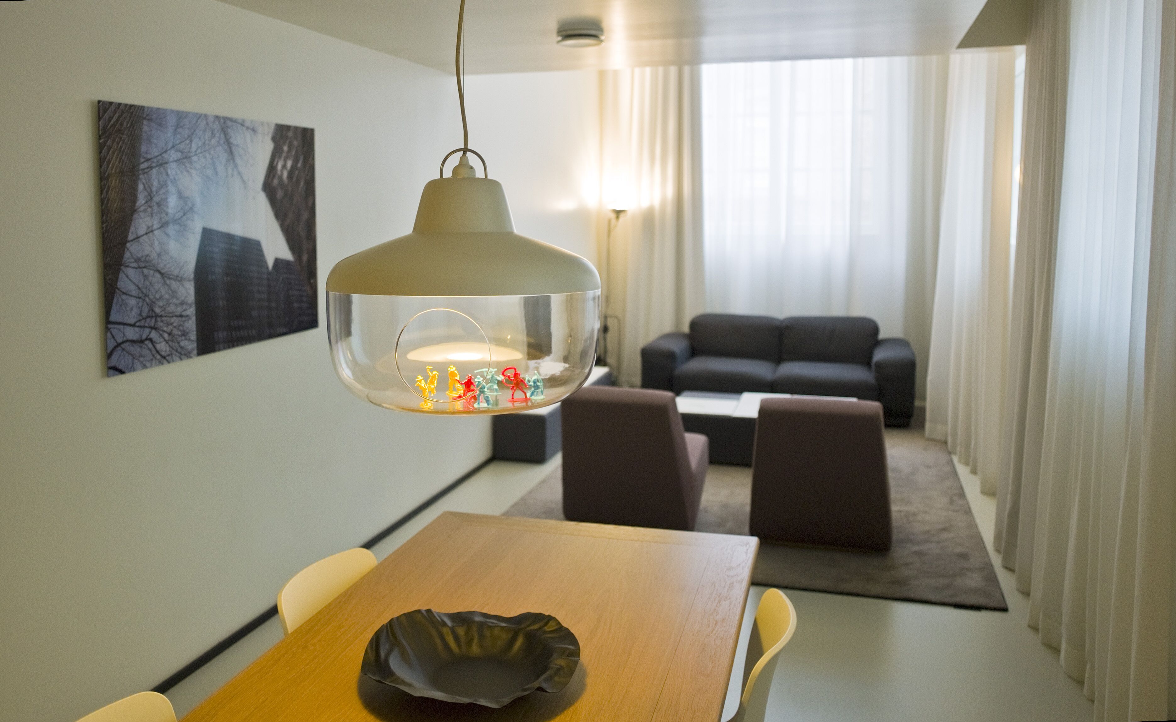 A modern hotel room with a dining area, a sofa, and a large window with curtains.