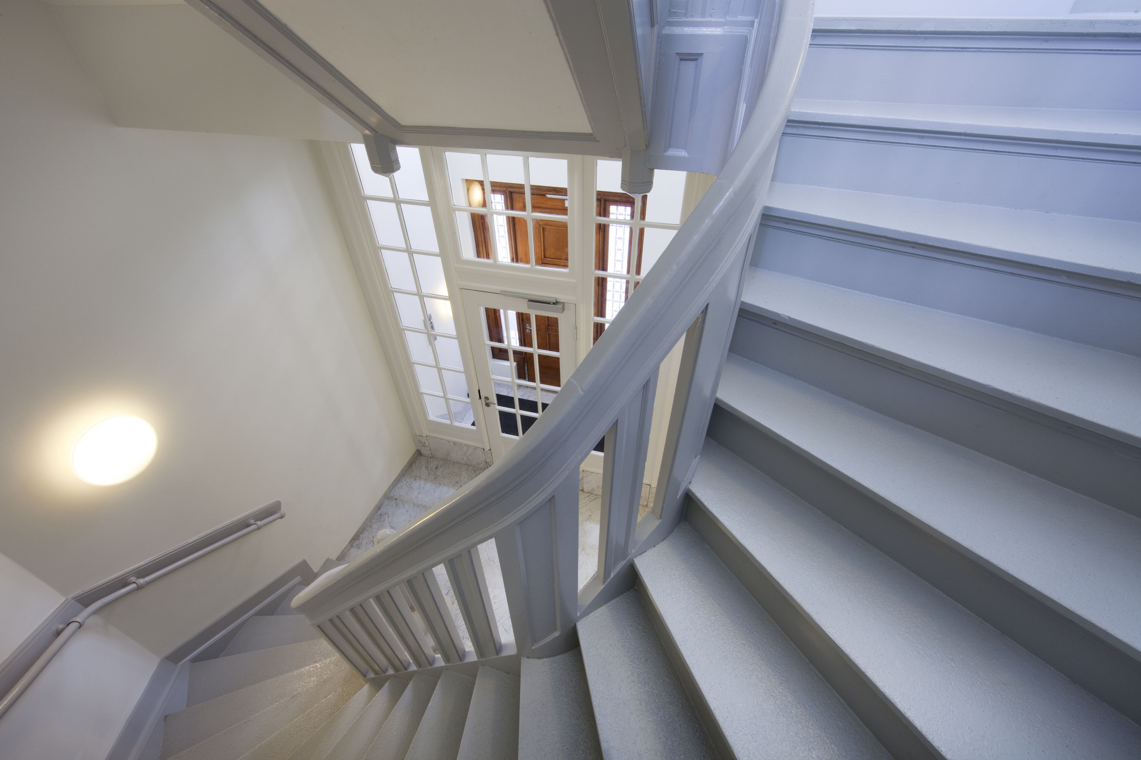 A staircase with white railings and a handrail, leading to a landing with a view of a wooden interior.