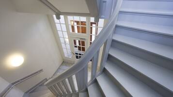 A staircase with white railings and a handrail, leading to a landing with a view of a wooden interior.