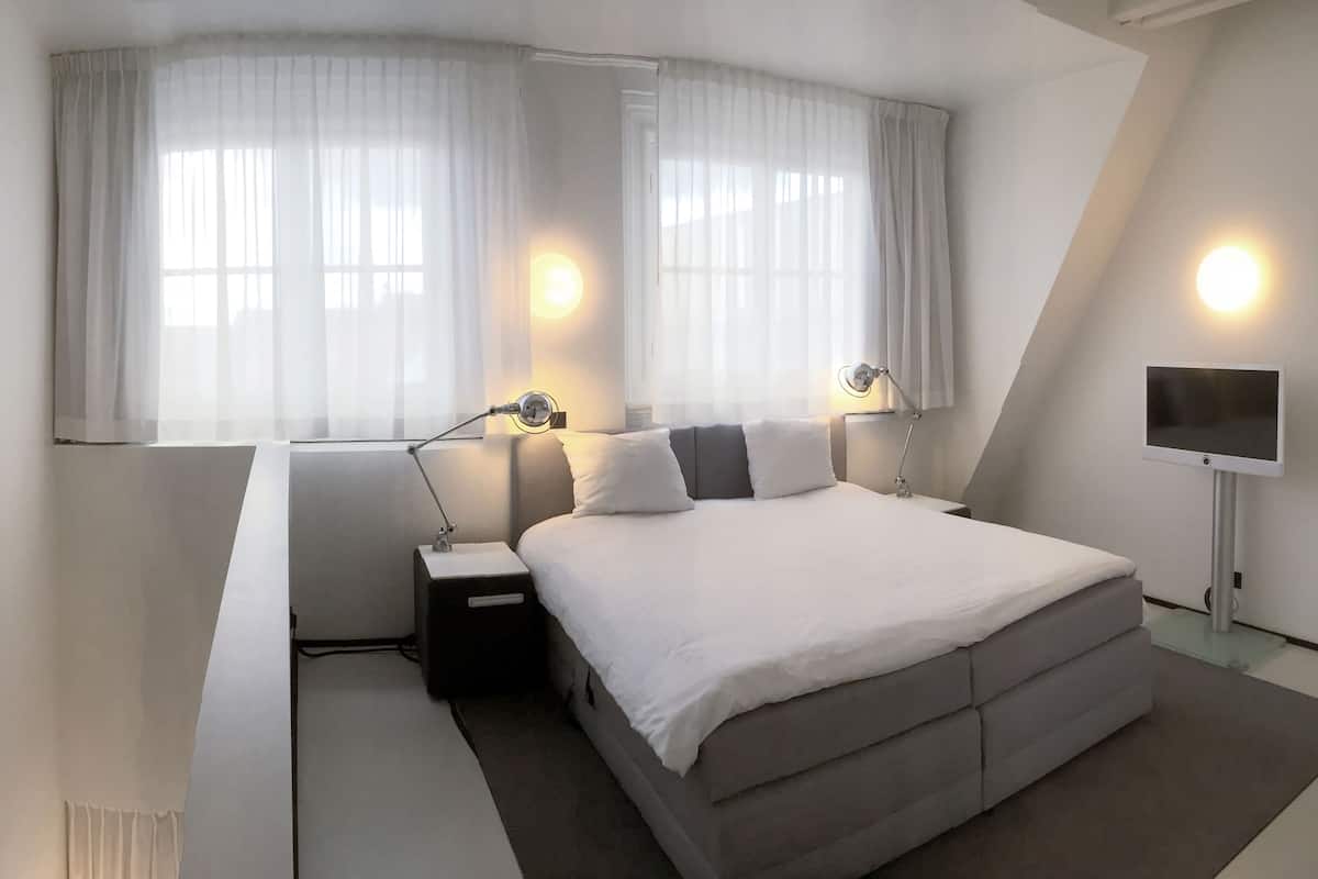 Ett modernt hotellrum med en stor säng, sänglampor, en platt-TV och en tavla på väggen.