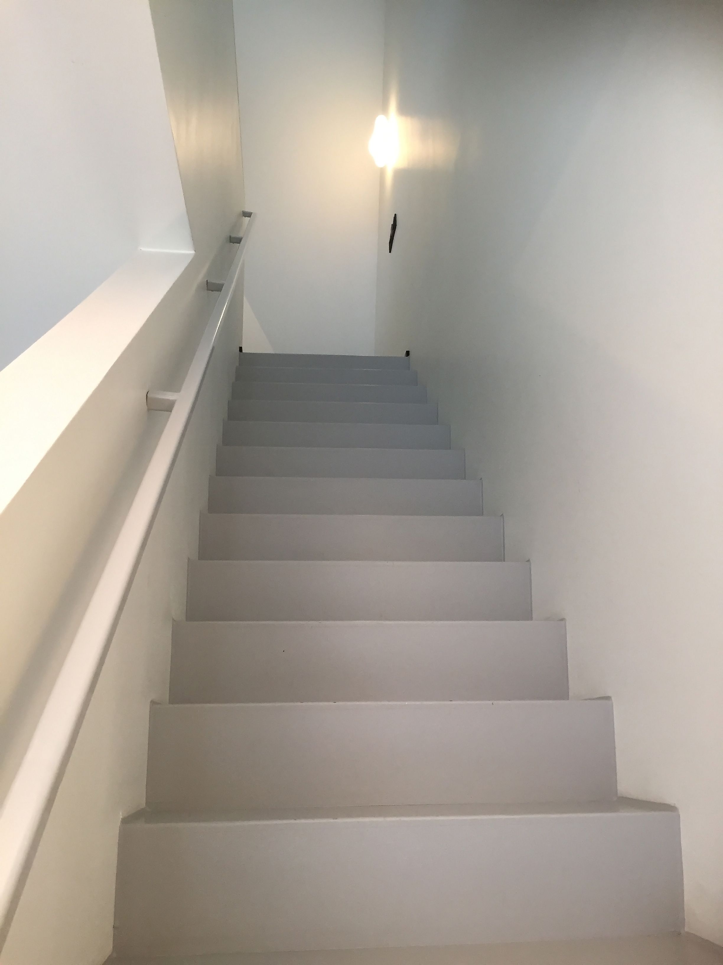 A staircase with white steps and a handrail, leading up to a landing with a light fixture.
