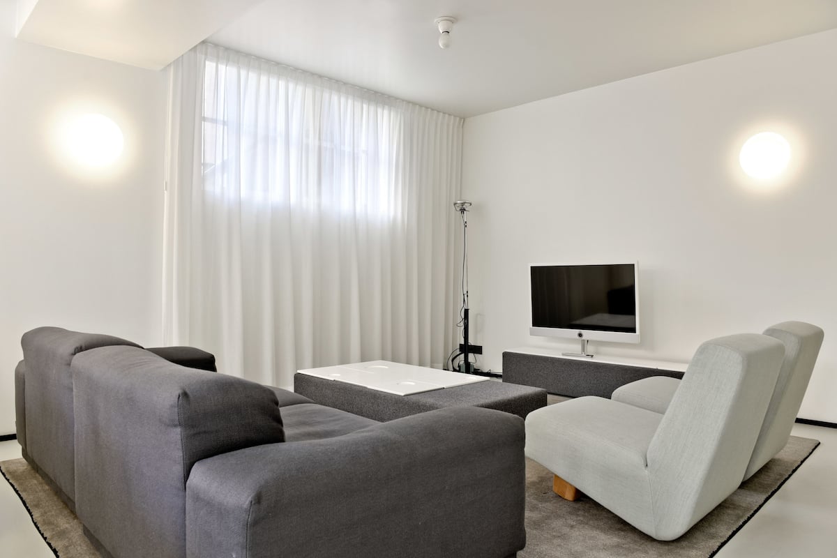 Ett modernt vardagsrum med en grå soffa, en ljusgrå fåtölj, en platt-TV och en golvlampa.