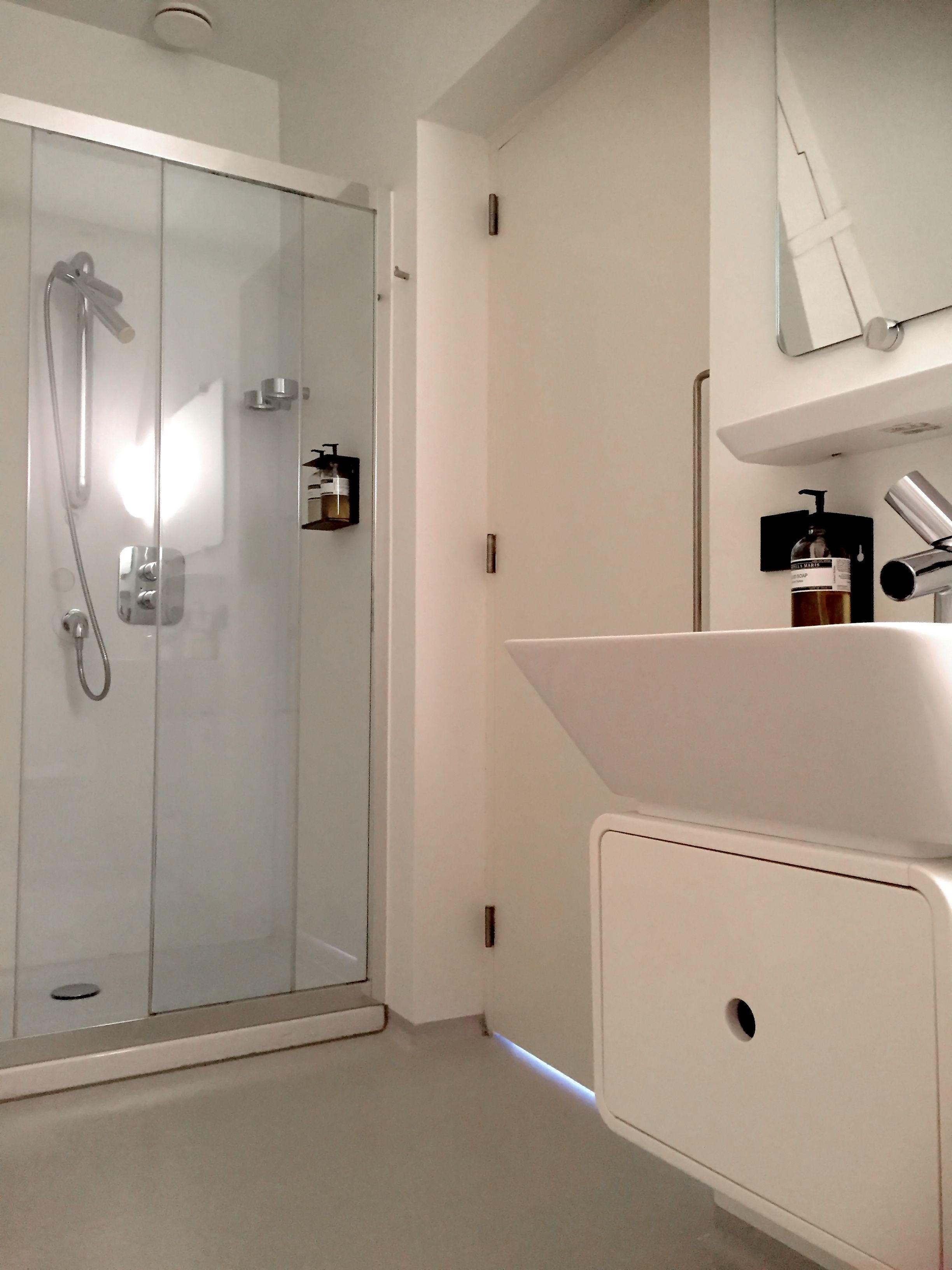 Ein modernes Badezimmer mit Duschkabine aus Glas, einem weißen Waschbecken und einem Spiegel darüber.