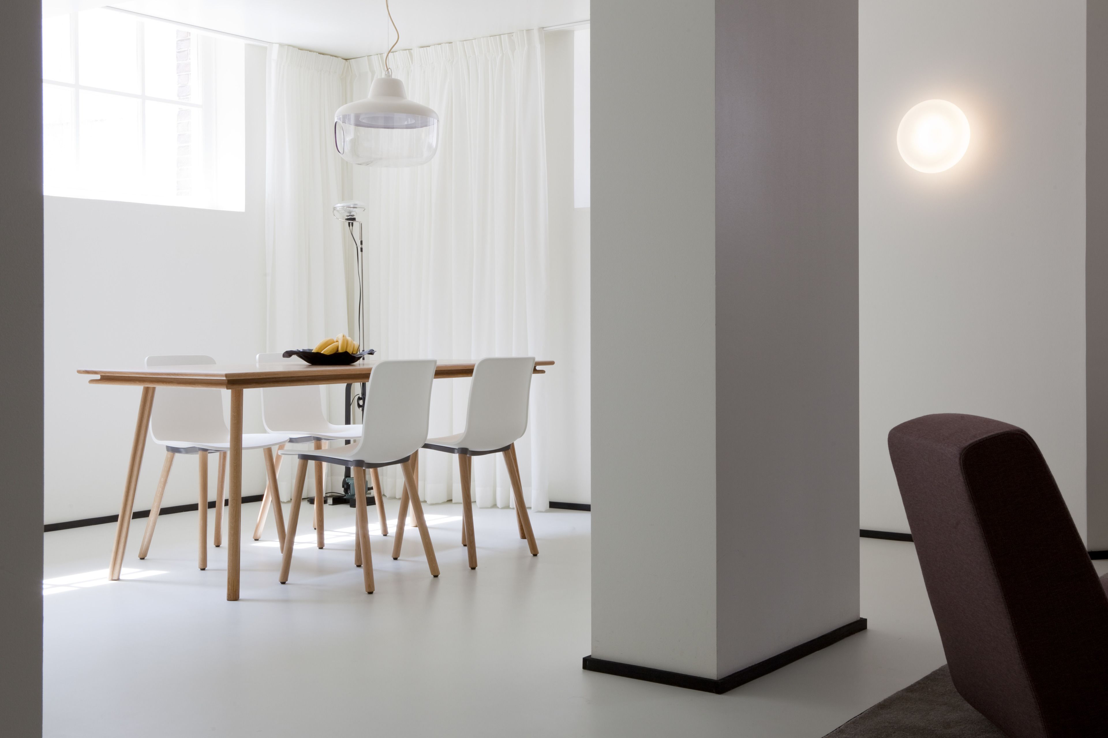 A modern dining area with a wooden table and white chairs, a pendant light, and a round wall light.