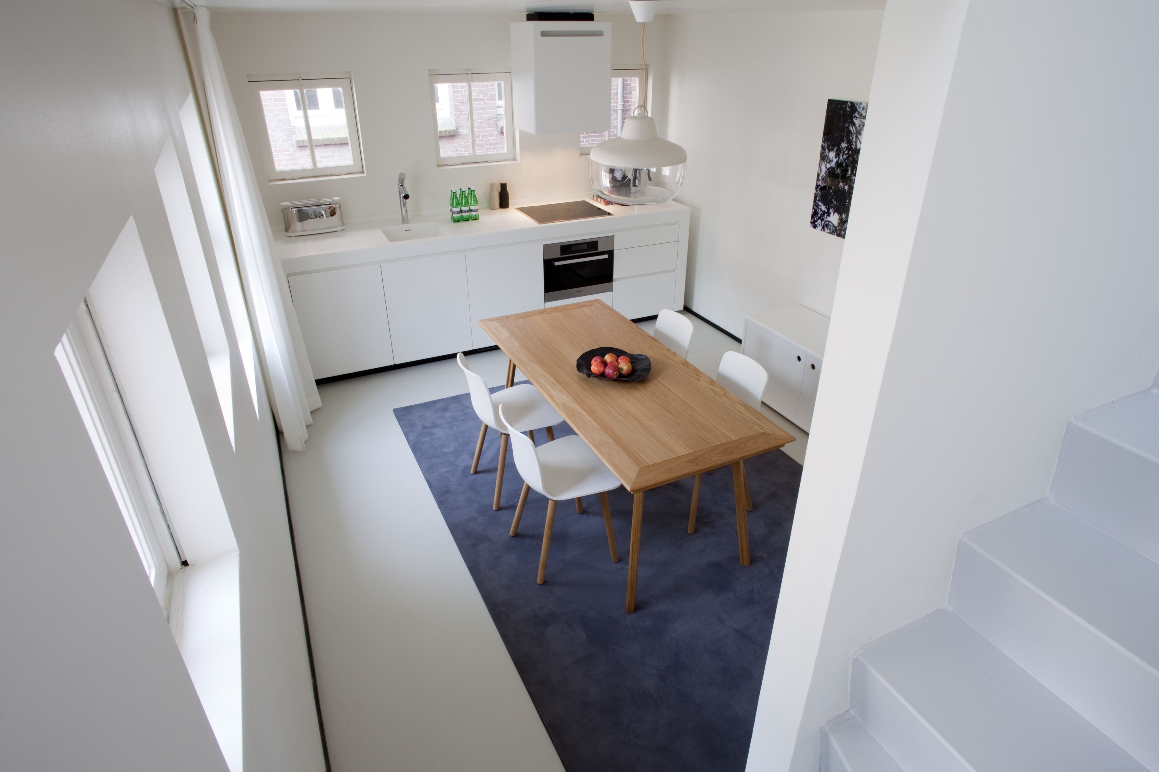 Una cocina moderna con armarios blancos, una mesa de comedor de madera y una alfombra azul.
