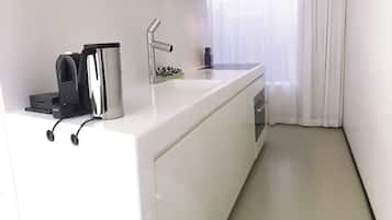 Een moderne keuken met een wit aanrecht, een ingebouwde koffiezetapparaat, een spoelbak en een raam met dunne gordijnen.
