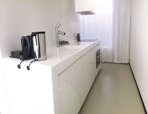 A modern kitchen with a white countertop, a built-in coffee maker, a sink, and a window with sheer curtains. - Urban Residences Maastricht (Maastricht)