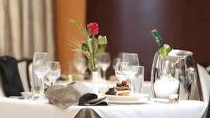 Una mesa lista para comer, con una jarrón de agua, una rosa y un plato de comida.