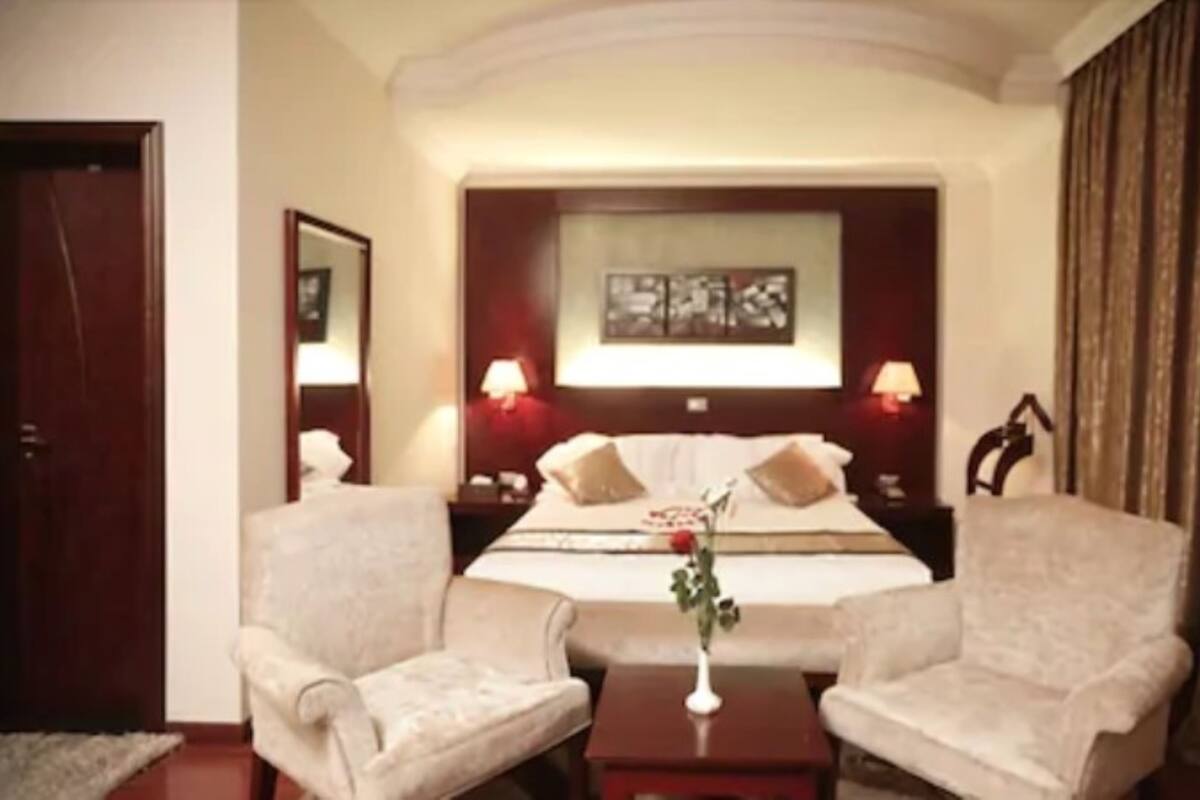 A hotel room with a large bed, two bedside tables with lamps, a small table with a vase, and two armchairs.