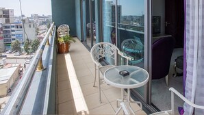 Un balcón con una mesa y sillas de vidrio, una planta en maceta y vistas de la ciudad.