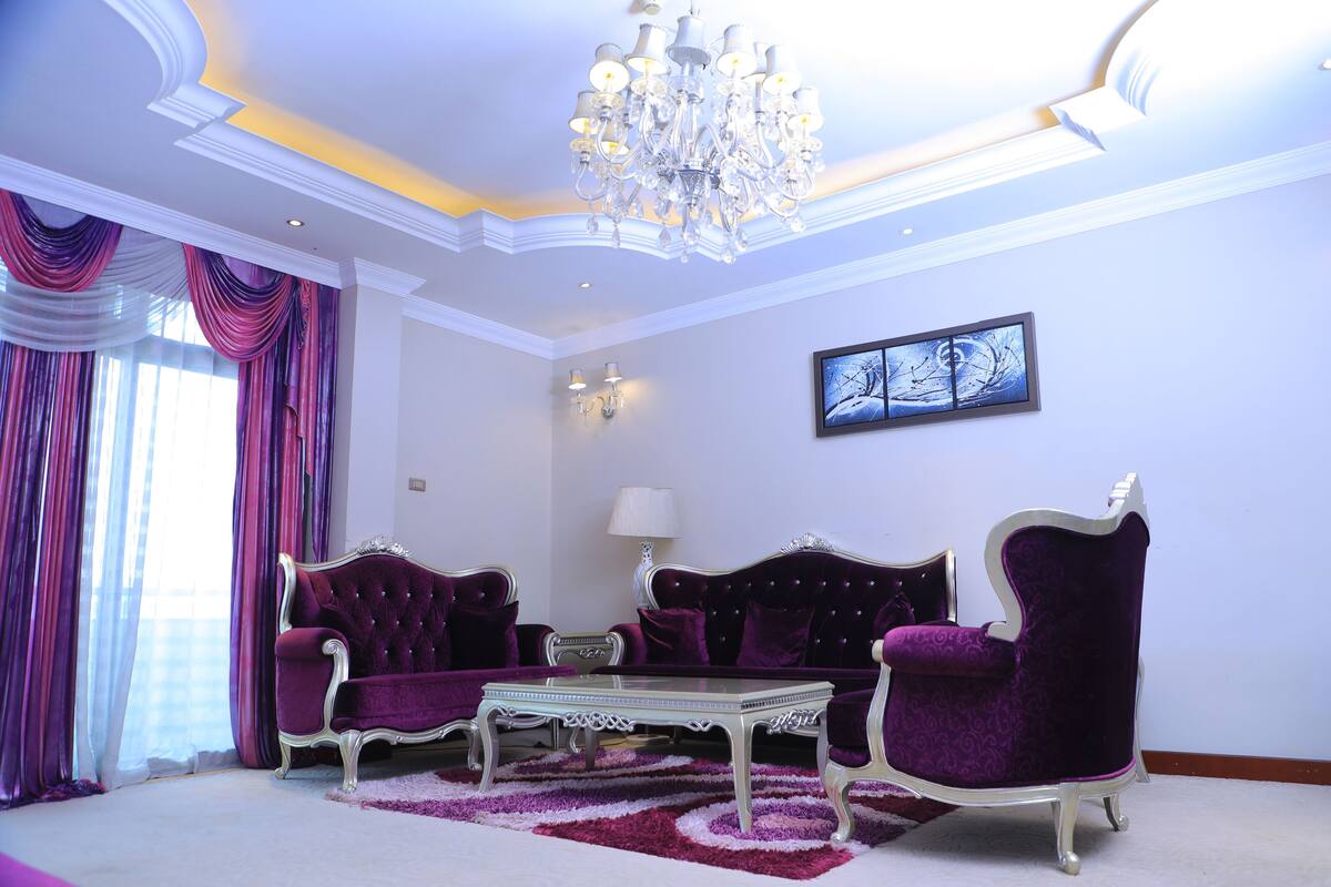 A luxurious living room with a chandelier, purple sofas, and a glass coffee table.