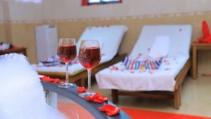 Una habitación con dos sillones, una cama y dos copas de vino tinto sobre una mesa.