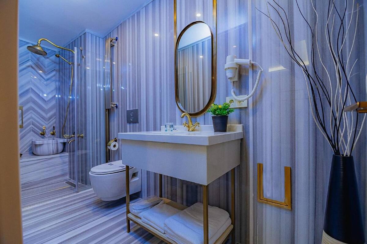 A modern bathroom with a marble floor, a white sink with gold fixtures, a large mirror, and a shower with a handheld showerhead.