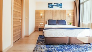 Una habitación de hotel moderna con una cama grande, cabecero de madera y un cuadro abstracto azul sobre ella.
