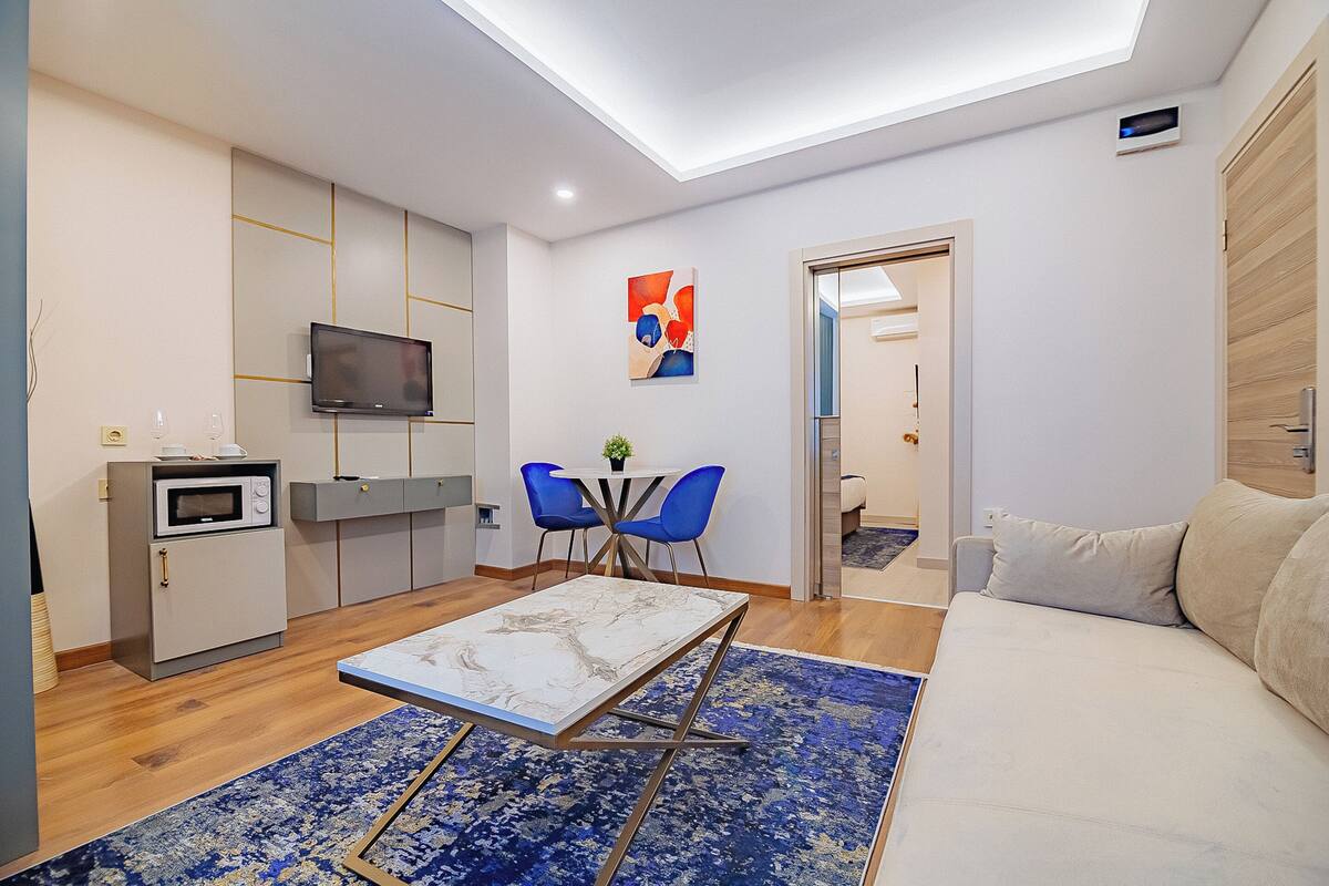 A modern living room with a sofa, a coffee table, a TV, and a dining area with chairs.