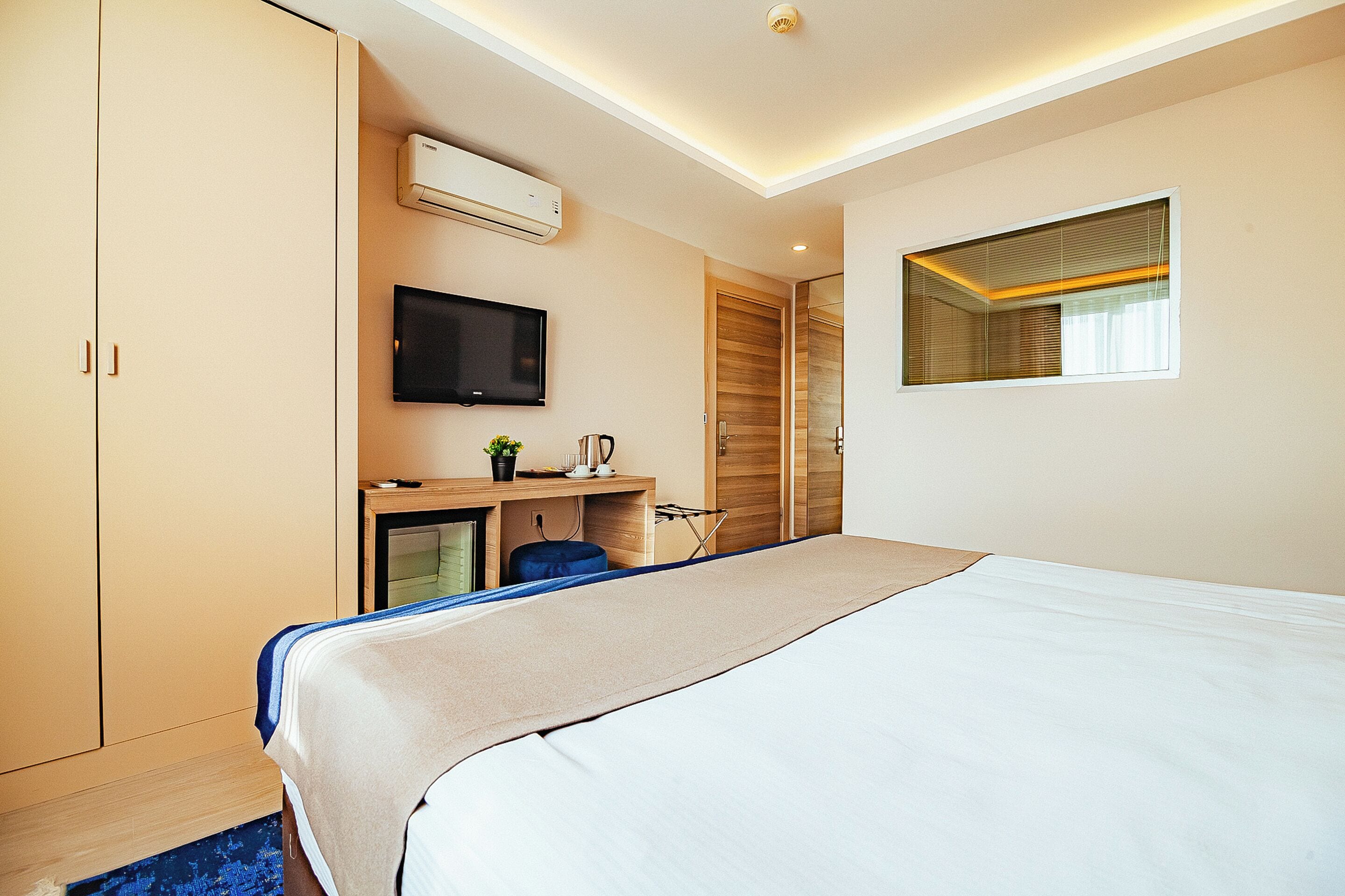 Una habitación de hotel moderna con una cama grande, un escritorio con una computadora, un televisor y un equipo de aire acondicionado.