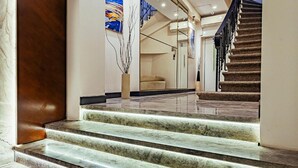 Un vestíbulo de hotel con escalones de mármol que conducen a una escalera, una recepción y un amplio ventanal con vistas.