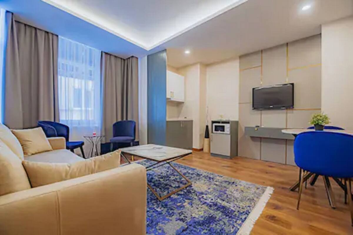 A modern living room with a sofa, blue chairs, a coffee table, and a kitchen area with a TV.