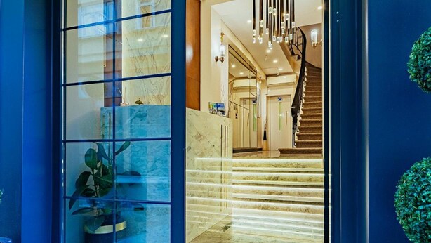 Un moderno vestíbulo de hotel con una escalera de mármol, una entrada con puerta de cristal y vistas del interior.