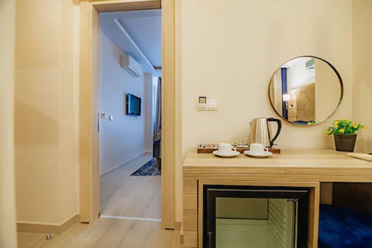 A hotel room with a wooden desk, a round mirror, a small potted plant, and a view of the hallway.