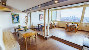 Una habitación con piso de madera, un sofá, una mesa de comedor con sillas y vistas a la ciudad a través de amplios ventanales.