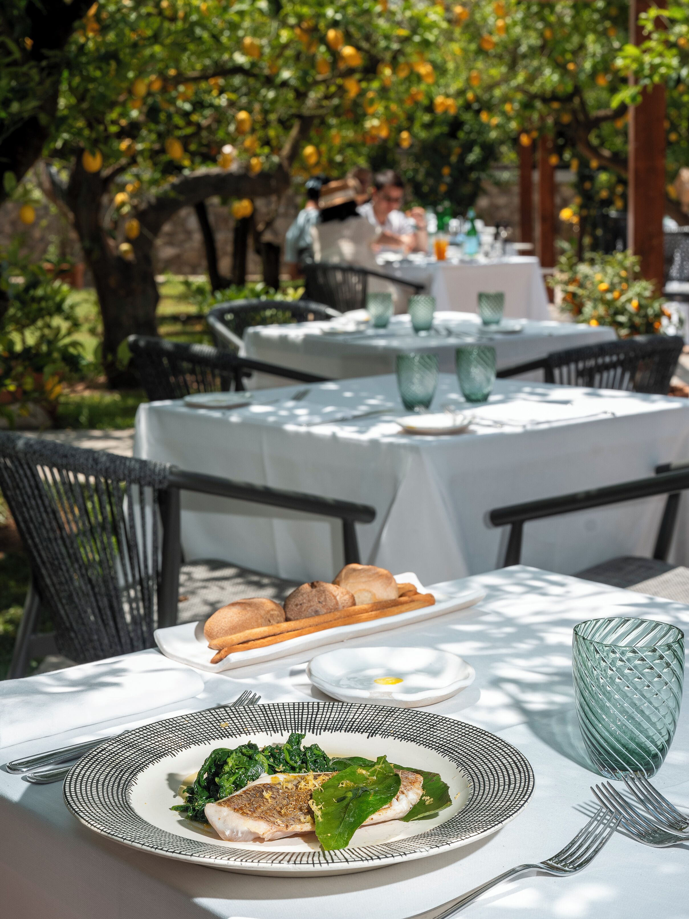 An outdoor dining area with round tables, chairs, and a variety of dishes including fish and bread.